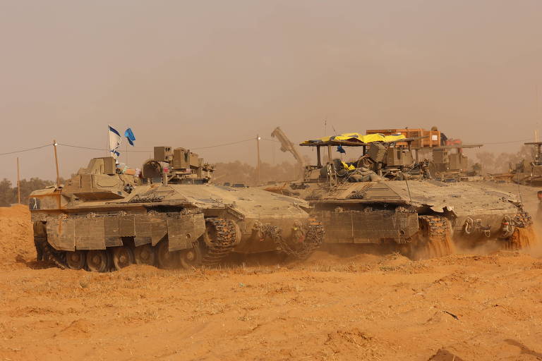 Veículos militares de Israel estão estacionados em um terreno árido; acima, um céu aparece envolto em uma névoa de poeira alaranjada