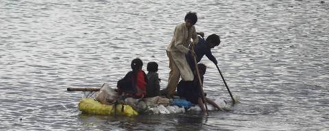 Children use a raft to make their way in a flooded area after heavy monsoon rains on the outskirts of Sukkur, Sindh province, on August 27, 2022. - Thousands of people living near flood-swollen rivers in Pakistan's north were ordered to evacuate on August 27 as the death toll from devastating monsoon rains neared 1,000 with no end in sight. (Photo by Asif HASSAN / AFP)