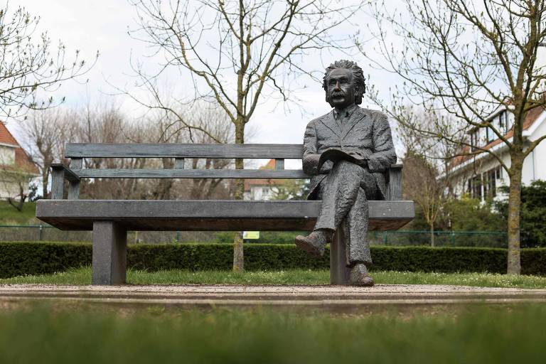 Uma estátua de bronze de uma pessoa sentada pensativamente em um banco de parque, cercada por um ambiente tranquilo com grama verde e árvores ao fundo