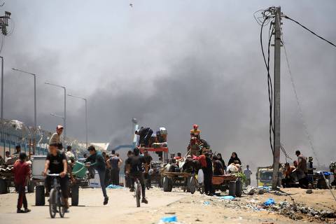 TOPSHOT - Palestinians flee with their belongings as smoke rises in the background, in the area of Tel al-Sultan in Rafah in the southern Gaza Strip on May 30, 2024, amid the ongoing conflict between Israel and the militant group Hamas. (Photo by Eyad BABA / AFP)