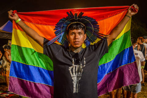 Indígena da etinia Boe Bororo segura bandeira do arco-íris, símbolo do Orgulho LGBTQIA+, durante programação cultural no Acampamento Terra Livre