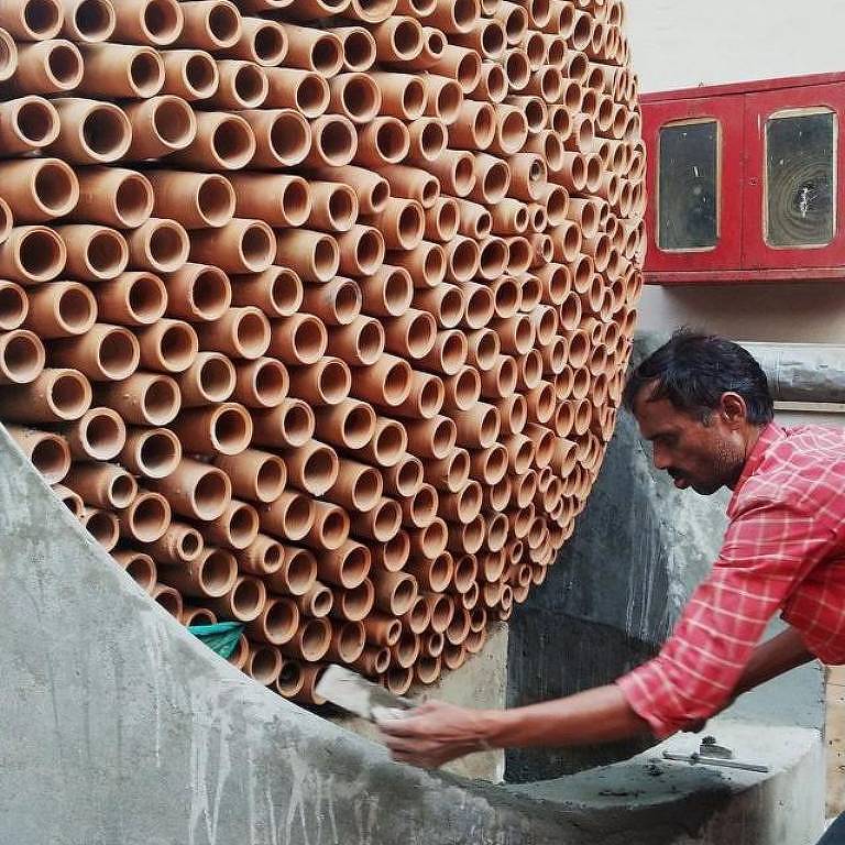 Um trabalhador indiano verifica a qualidade de tubos de cerâmica empilhados.