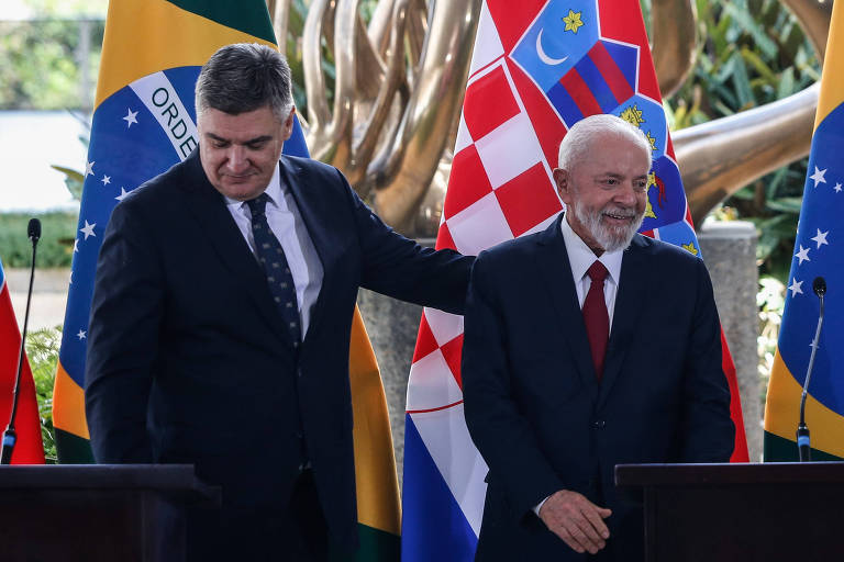 Lula e o presidente da Croácia estão lado a lado evento formal, com bandeiras dos dois países ao fundo