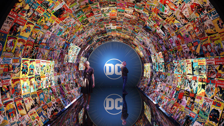 Um corredor recebe a logo da DC Comics ao fundo, no centro de um túnel, que é adornado com uma colagem colorida de capas de quadrinhos