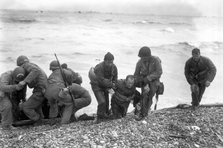 Soldados americanos ajudam colegas que sobreviveram a um naufrágio na praia de Utah