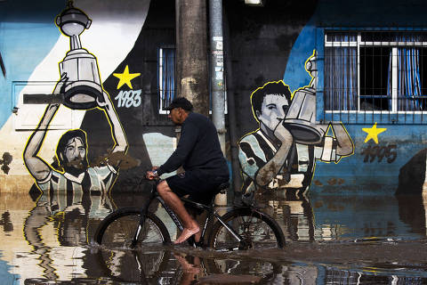 A man rides a bicycle on a flooded street around the Arena do Gremio stadium in Porto Alegre, Rio Grande do Sul state, Brazil, on May 29, 2024. The water and mud have rendered Gremio and Internacional's stadiums and headquarters inoperable. Without places to train or play football, the Brazilian clubs became itinerant teams to avoid the floods that ravaged southern Brazil. (Photo by SILVIO AVILA / AFP)