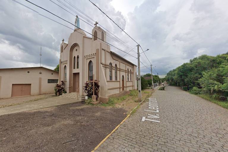 Uma pequena igreja com arquitetura clássica repousa pacificamente ao lado de uma rua pavimentada com paralelepípedos, em um dia nublado