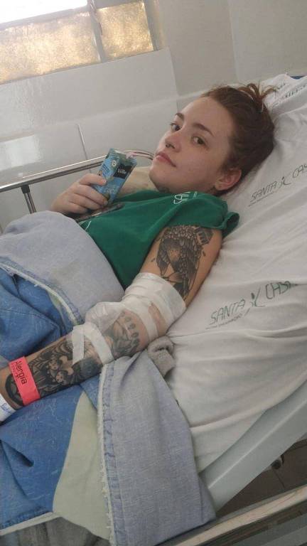 Carolina deitada em cama de hospital tomando suco de caixinha