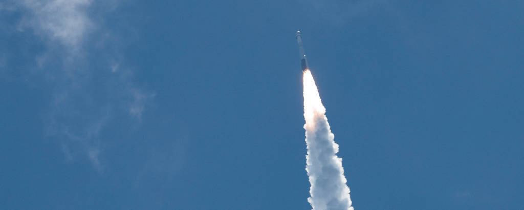 Um foguete branco corta o céu azul claro, deixando um rastro de fumaça em sua jornada rumo ao espaço
