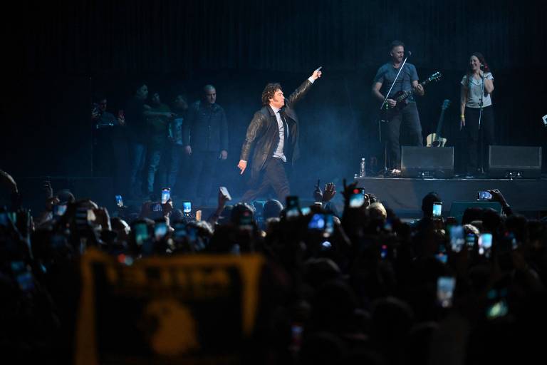 O presidente argentino, Javier Milei dança no palco do Luna Park em um concerto ao vivo para lançamento de seu novo livro, cercado por músicos e banhado pela luz dos holofotes, enquanto uma multidão de fãs captura o momento em seus celulares, criando um mar de telas iluminadas
