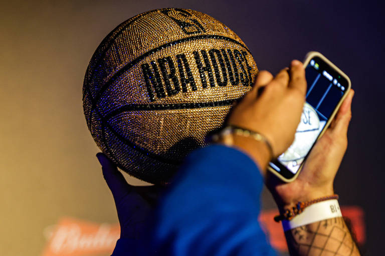 Uma pessoa segura um smartphone e tira fotos de uma bola de basquete da NBA cravejada de pedras brilhantes