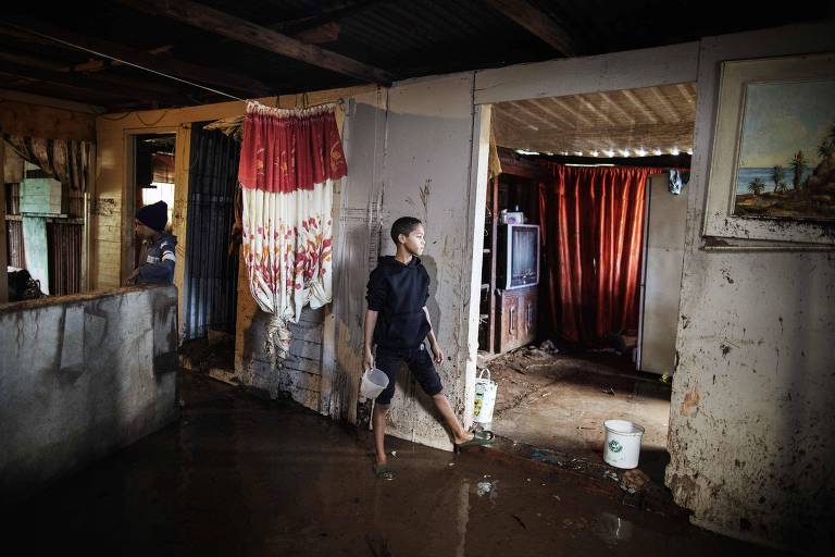 Criança limpa a água da enchente em sua casa em Uitenhage, África do Sul