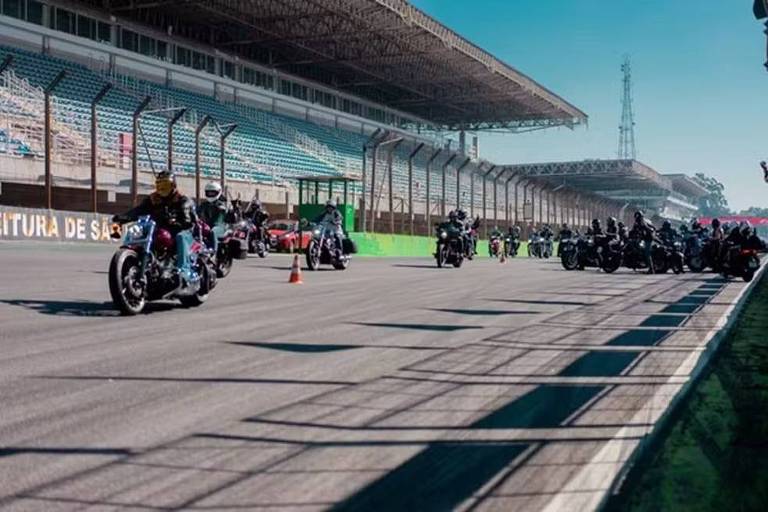 Imagem de um trecho reto do Autódromo de Interlagos. As arquibancadas podem ser vistas à esquerda, mas elas estão vazias. O dia está ensolarado e diversos motoqueiros estão dirigindo suas motos na pista