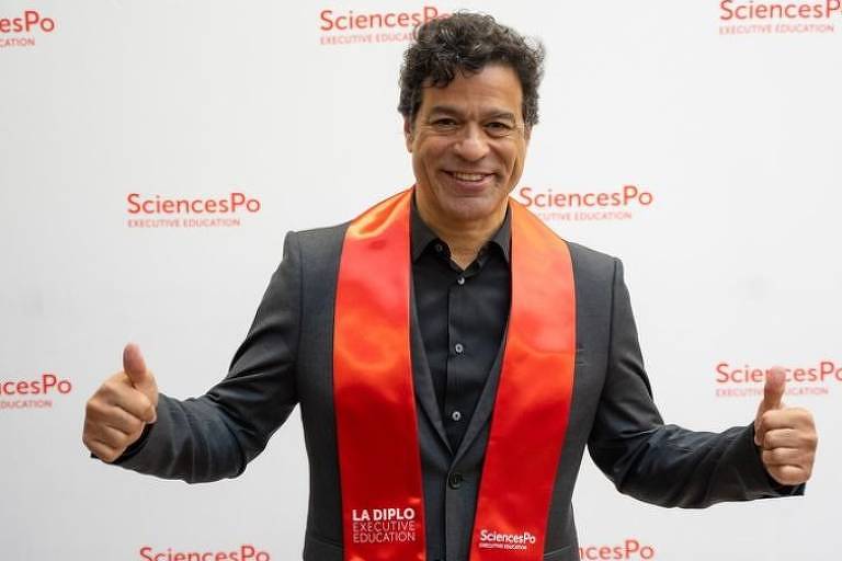 Em foto colorida, homem comemora ter recebido o diploma em uma universidade
