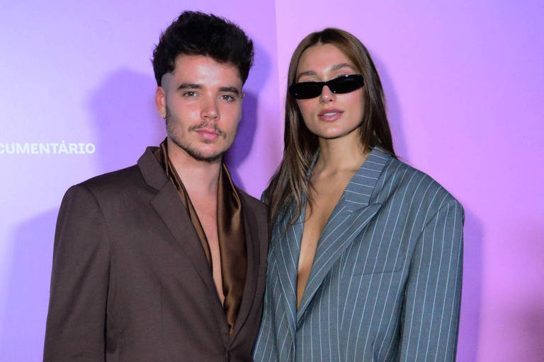 Sasha Meneghel e João Figueiredo posam usando blaser marrom e cinza, respectivamente