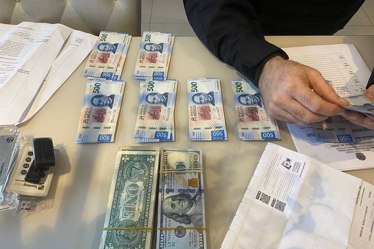 Mesa com cédulas de dólar e peso mexicano dispostos em pilha com mão que segura notas