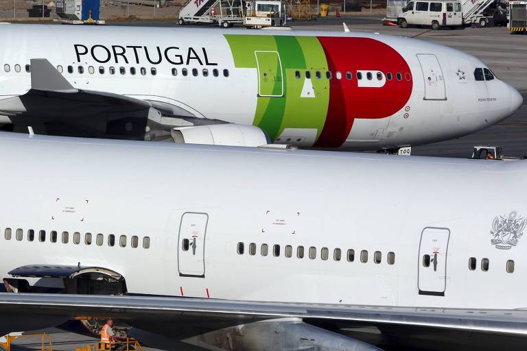 A imagem mostra dois aviões estacionados lado a lado em uma pista de aeroporto. Os aviões são grandes e brancos, com o modelo ao fundo exibe a marca da TAP Air Portugal pintada em verde e vermelho e branco. Eles têm motores embaixo das asas e caudas longas e finas.