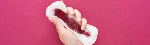 Vista parcial da mulher segurando absorvente com sangue no fundo roxo