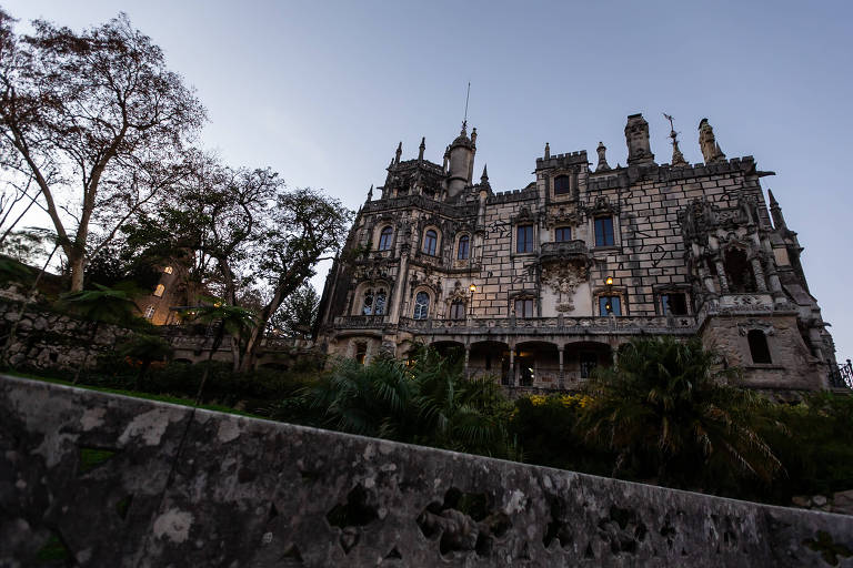 Imagem geral mostra edificação da Quinta em meio a natureza; muro de pedra em declive em primeiro plano e vegetação no entorno.