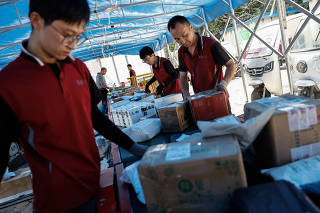 Delivery workers sort packages on a conveyor belt, ahead of the 
