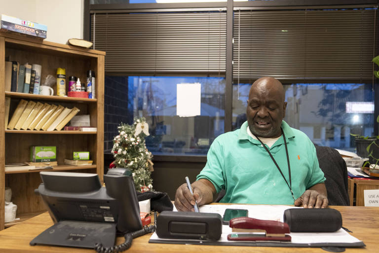 Um homem negro trabalha em sua mesa repleta de papéis e telefones