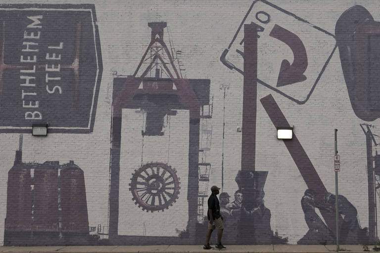 Um transeunte observa um grande mural que homenageia a história industrial, com destaque para a Bethlehem Steel, uma vez uma gigante da indústria do aço. O mural apresenta imagens estilizadas de equipamentos e ferramentas, evocando a era do poder industrial.