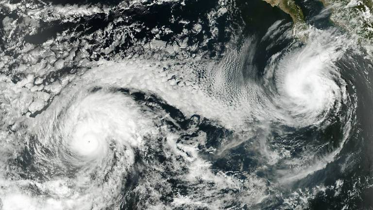 Imagem de satélite captura a visão de dois ciclones em formação, vistos do espaço. As massas de nuvens espiraladas dominam a cena.