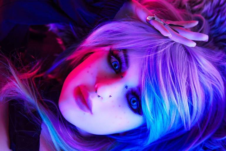 Uma pessoa criada por IA, com maquiagem repousa sob luzes de neon. A luz azul e roxa destaca os contornos do rosto e os detalhes da maquiagem.