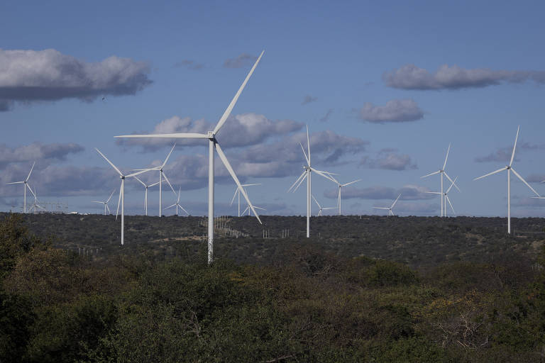 Um parque eólico se destaca contra um céu azul parcialmente nublado, com várias turbinas eólicas alinhadas no horizonte.