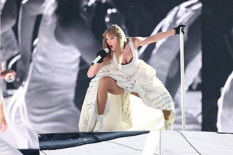 Uma mulher loira segura microfone e canta usando uma roupa toda branca em cima de um palco musical