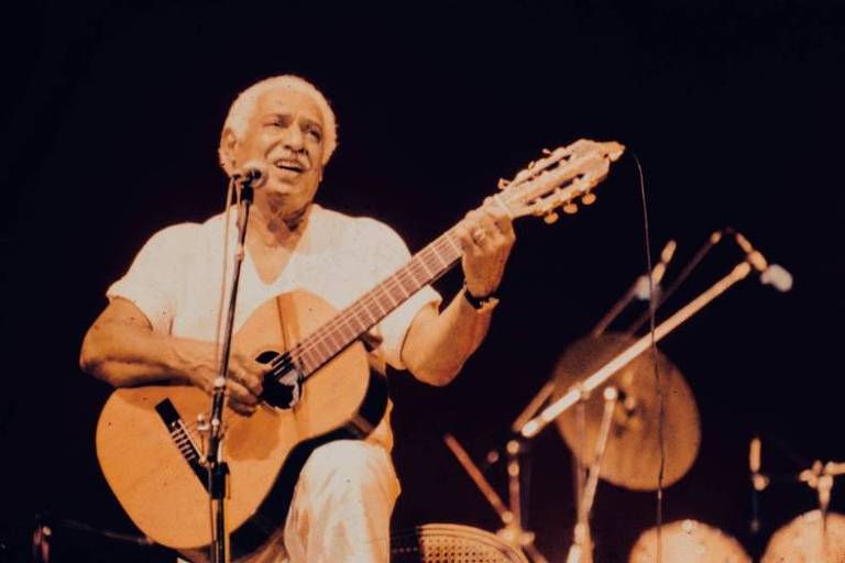 Em foto colorida, Dorival Cammi aparece tocando violão e cantando