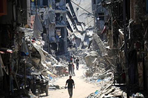 TOPSHOT - Palestinian men walk along a narrow street past destroyed buildings in Khan Yunis, in the southern Gaza Strip on June 11, 2024, amid the ongoing conflict between Israel and the Palestinian Hamas militant group. (Photo by Eyad BABA / AFP)
