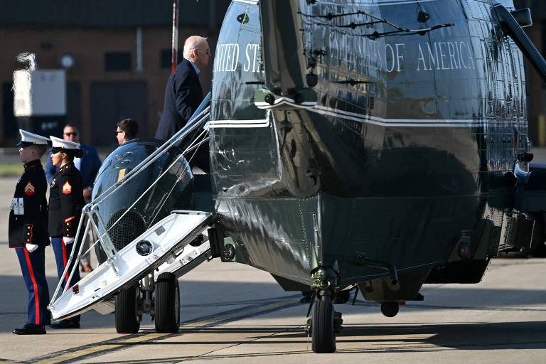 Um indivíduo está embarcando em um helicóptero com a inscrição "United States of America". A cena é vigiada por membros da Marinha dos EUA em uniforme de cerimônia, destacando a importância do passageiro e a formalidade do momento.