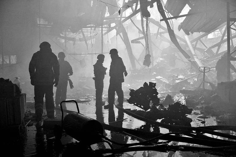 Imagem em preto e branco mostra bombeiros em um prédio arruinado, com água pelo chão