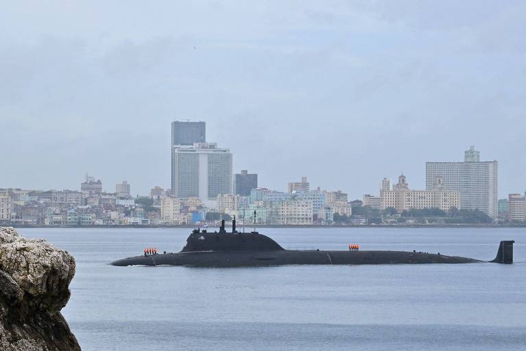 Submarino escuro navega com a cidade de Havana ao fundo. O tempo está nublado