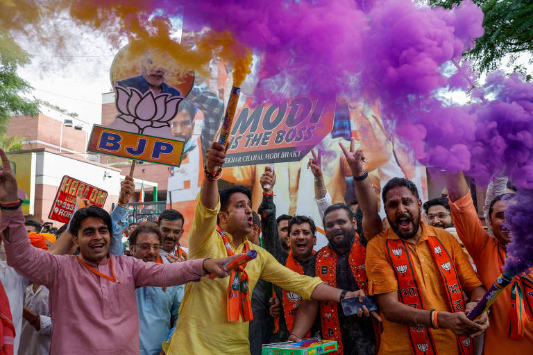 Grupo de homens vestidos de laranja e amarelo, levando placas com os dizeres "BJP"e "Modi is the boss", comemoram, com fumaça roxa visível na foto 