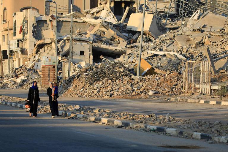 Palestinos andam próximos de edifícios destruídos em Al-Bureij, no centro de Gaza
