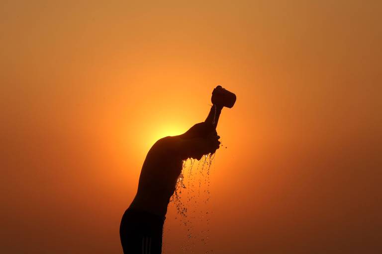 Silhueta de homem jogando água na cabeça com uma caneca; ao fundo, o sol está gigante, laranja, tomando conta de toda a imagem