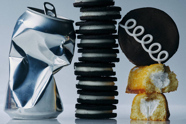 Uma lata de refrigerante prateada e uma pilha de biscoitos recheados preto e branco parecem interagir em um fundo neutro, criando uma cena que personifica o prazer de combinar lanches doces e bebidas refrescantes.
