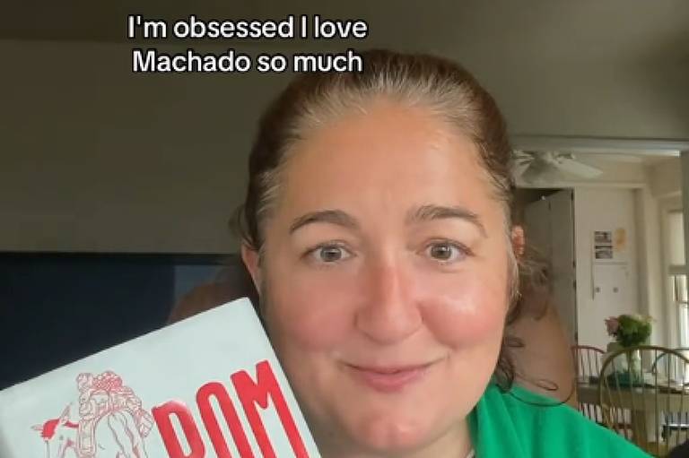 Uma mulher de cabelos escuros segura um exemplar do livro "Dom Casmurro", de Machado de Assis. No canto superior da imagem, está escrito "Capitu traiu?", em referência à personagem protagonista do livro. 