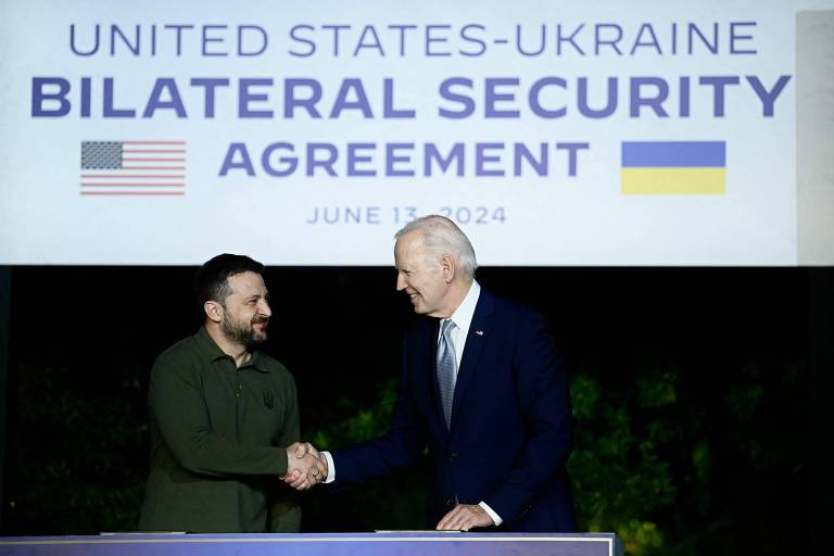 Dois líderes políticos apertam as mãos diante de um pano de fundo que anuncia um acordo de segurança bilateral entre os Estados Unidos e a Ucrânia, simbolizando um momento de cooperação e parceria estratégica entre as duas nações.