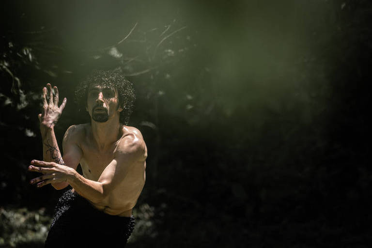 Um homem branco sem camisa dança na floresta