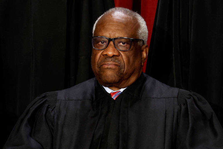 Thomas, um homem negro vestindo uma toga de juiz, senta-se com uma postura ereta e expressão contemplativa