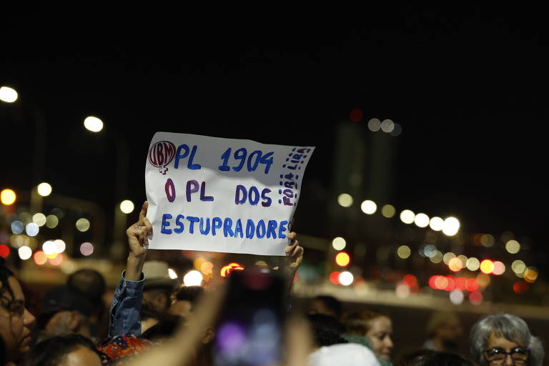 Protesto em Brasília, durante à noite; no destaque, mulher ergue cartaz com os dizeres: "PL 1904, o PL dos estupradores"