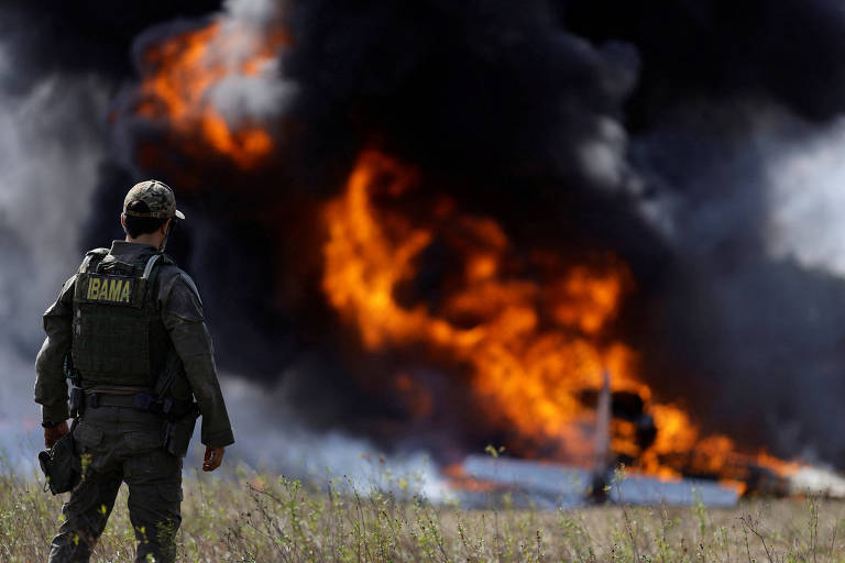 De costas para a câmera, fiscal do Ibama observa avião de garimpeiros queimando. Enormes labaredas e fumaça escura tomam o céu 