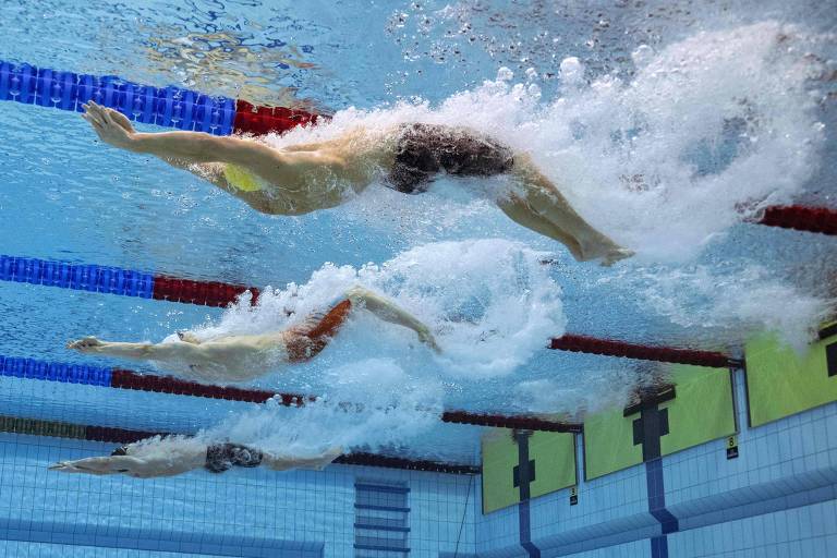 Dois nadadores em competição, capturados abaixo da superfície da água, mostram a intensidade e a técnica do nado livre. As bolhas de ar e as ondas criadas pelos movimentos vigorosos dos atletas destacam a velocidade e o esforço envolvidos na prova