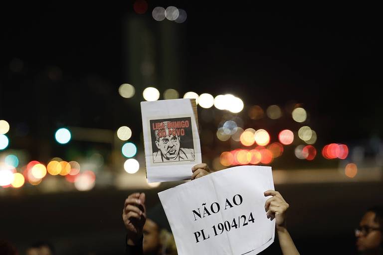 Mão de mulher seguram placa com a frase "Não ao PL 1904" durante um protesto que aconteceu a noite.