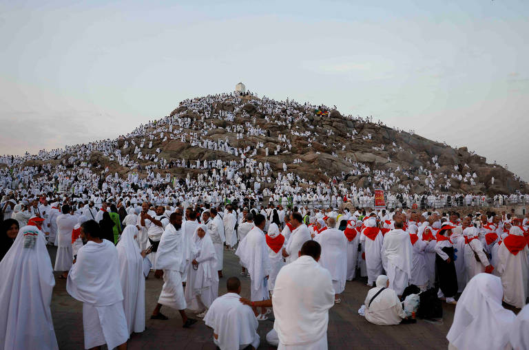 Uma multidão de pessoas vestindo túnicas brancas cerca um monte.