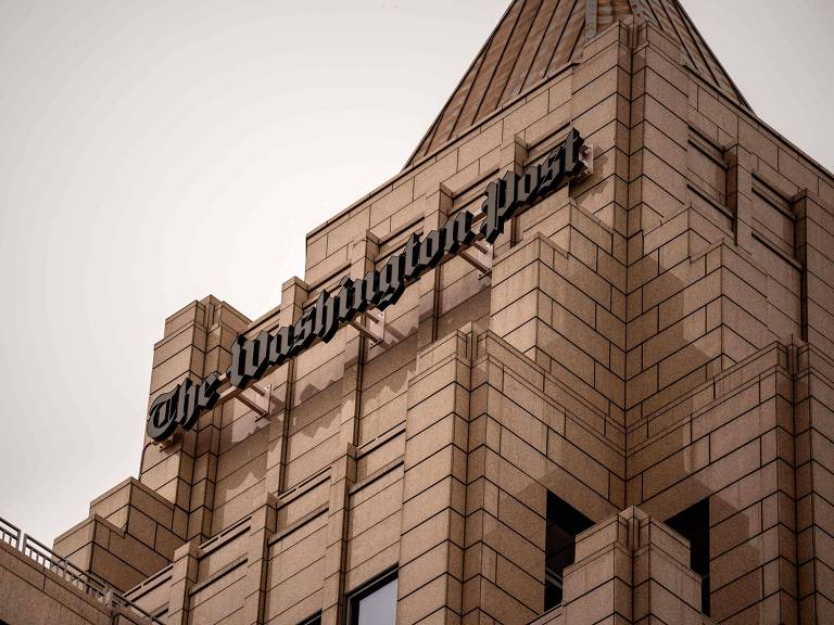 Fachada do prédio do jornal The Washington Post. Foto destaca a parte superior do prédio, composta por blocos beges, e o letreiro com o nome do veículo