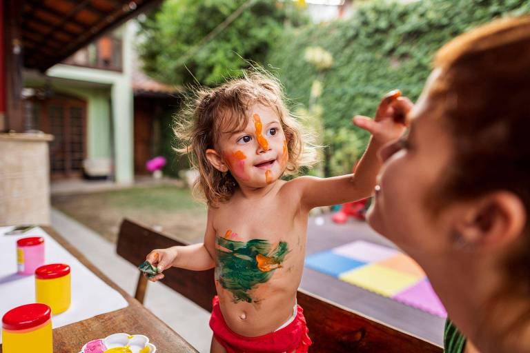 Criança brincando de pintar corpo dela e rosto da mãe
